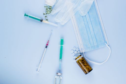 Top view of syringes, blue hygienic protective mask, gloves, tablets and glass medicine bottle ready for use. Pandemic and health concept.