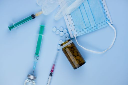 Top view of syringes, blue hygienic protective mask, gloves, tablets and glass medicine bottle ready for use. Pandemic and health concept.