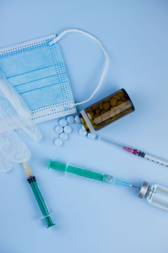 Top view of syringes, blue hygienic protective mask, gloves, tablets and glass medicine bottle ready for use. Pandemic and health concept.