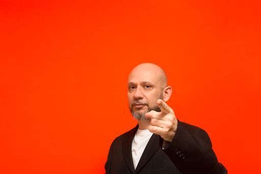 Business man, bald and bearded, intelligent, points to the camera. Isolated on orange background.
