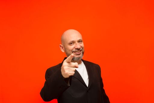 Business man, bald and bearded, intelligent, points to the camera. Isolated on orange background.