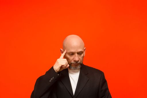 Business man, wearing black suit jacket, smart and thoughtful. Isolated on orange background.