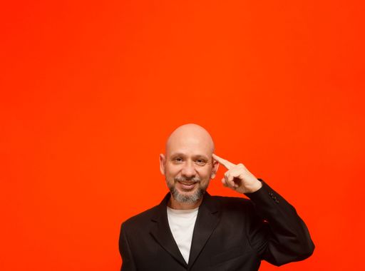 Business man, wearing black suit jacket, smart and thoughtful. Isolated on orange background.