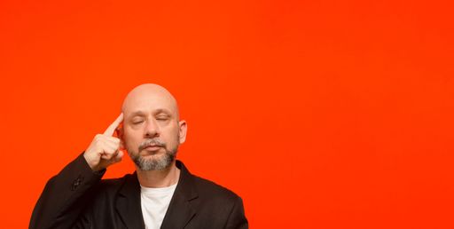Business man, wearing black suit jacket, smart and thoughtful. Isolated on orange background.