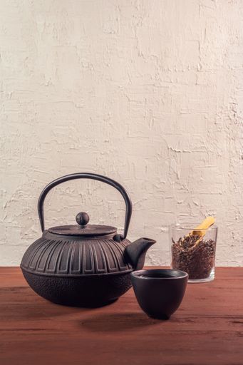 A vertical shot of a Japanese iron cast teapot, traditional ceramic teacup filled with black tea and loose black tea in a jar