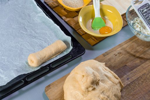 A closeup of uncooked pastry in an oven tray with egg yolk and pastry brush in a bowl