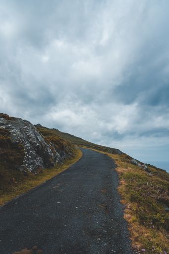A vertical shot of a road on the hill with nobody walking under the cloudy sky