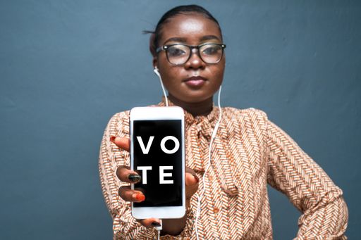 A closeup shot of a young lady wearing headphones holding her phone with writing "Vote"