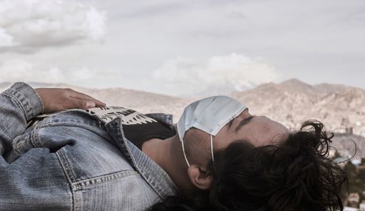 A young Hispanic man wearing a facemask, lying down outdoors during the covid-19 pandemic