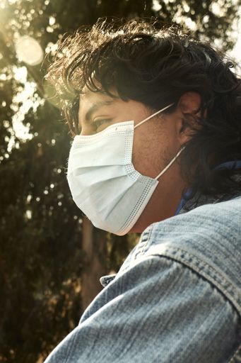A vertical shot of a young Hispanic man wearing a facemask, outdoors during the covid-19 pandemic
