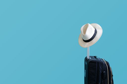 A closeup of a small Panama hat on a suitcase figure isolated on a blue background - holidays concept
