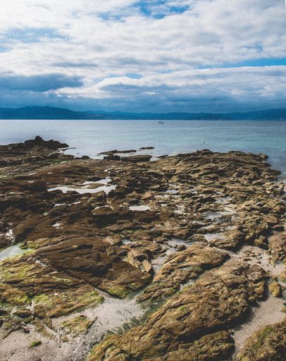 A vertical shot of rock formations near the sea under the cloudy sky