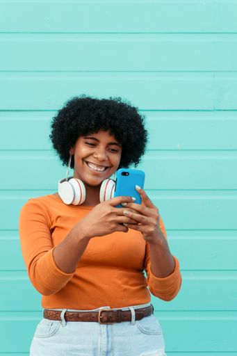 A vertical shot of a young attractive lady wearing headphones using her phone