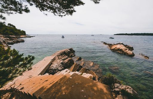 A landscape of a sea with boats surrounded by rocks with hills covered in forests on the background