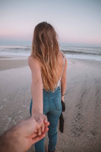 A vertical shot of a girl walking at the beach at sunset