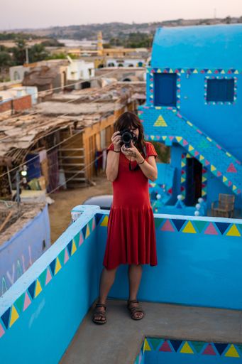 A vertical shot of a caucasian woman photographing in a traditional blue house in a Nubian village, in Egypt