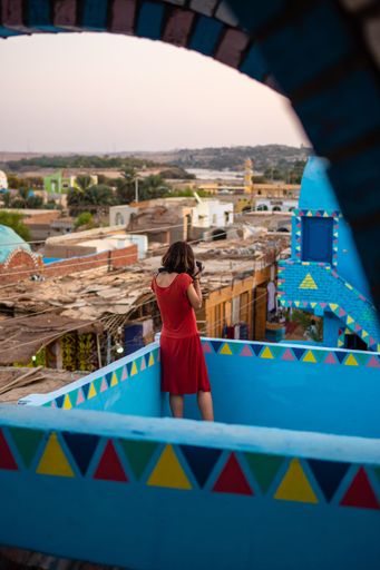 A vertical shot of a caucasian woman photographing in a traditional blue house in a Nubian village, in Egypt