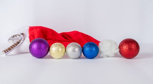 Some colorful Christmas ornaments and a Santa Claus hat on a white surface