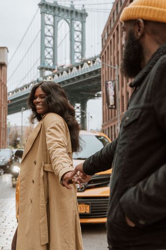 A couple holding each other's hand while walking against the Brooklyn Bridge in New York, USA