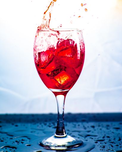 A vertical shot of ice splashing into a glass of red alcohol
