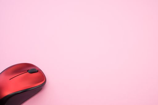 A high angle shot of a wireless mouse on a pink surface