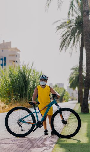 A vertical shot of a cyclist teenager wearing a mask and posing on a sunny day