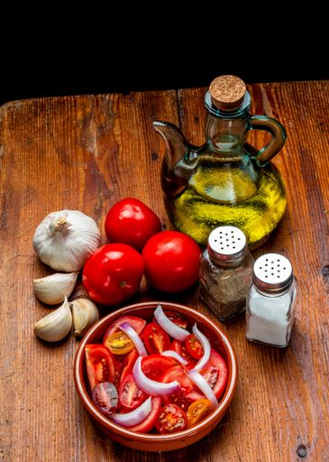 A fresh tomato, onion and olive oil salad in a bowl and ingredients on a wooden table