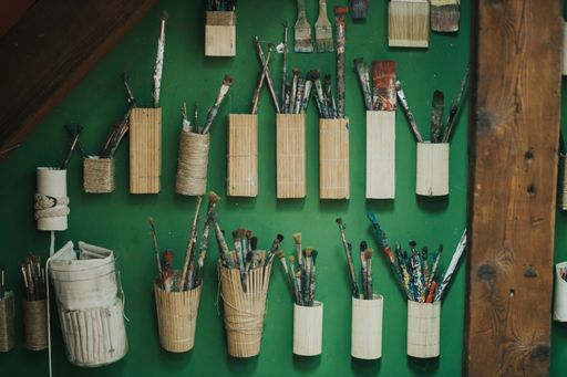 A selective focus shot of several paintbrushes in white jars on a green background