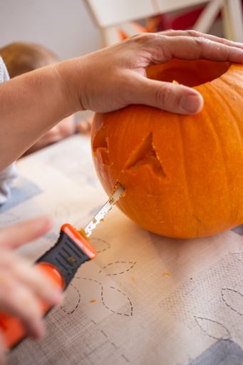 A closeup shot of a female's hand carving a pumpkin head for Halloween