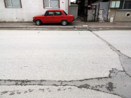 A red car parked by an old building on a street