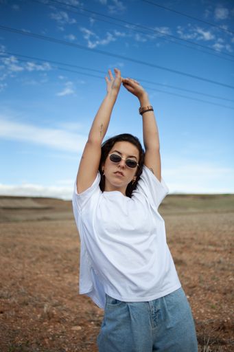 A vertical closeup portrait of a hipster cool Hispanic woman in stylish fancy sunglasses posing with her hands up in the air