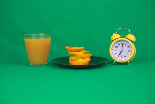 A closeup of slices of fruits on a plate with a cup of orange juice and a yellow clock
