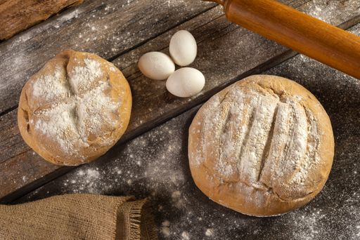 A top view of freshly baked homemade crusty pieces of bread with a rolling pin and eggs on a wooden board
