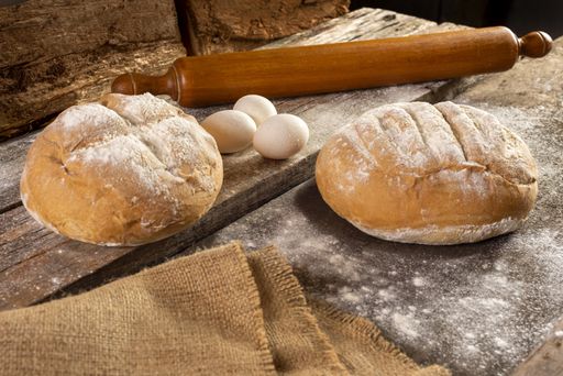 A freshly baked homemade crusty pieces of bread with a rolling pin and eggs on a wooden board