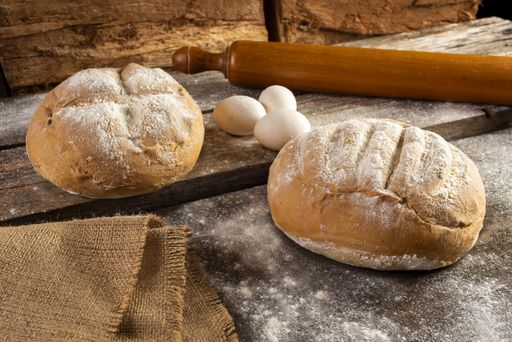 A freshly baked homemade crusty pieces of bread with a rolling pin and eggs on a wooden board
