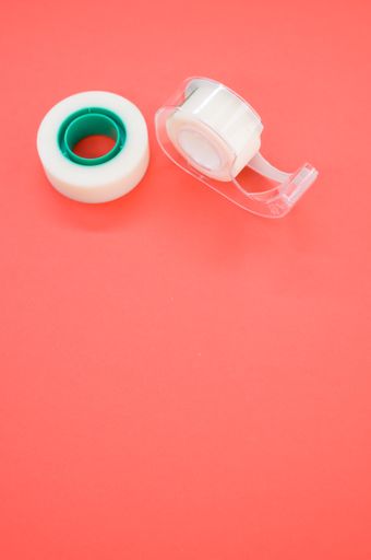 A top view closeup of a white duct tape and a tape dispenser isolated on a bright pink background