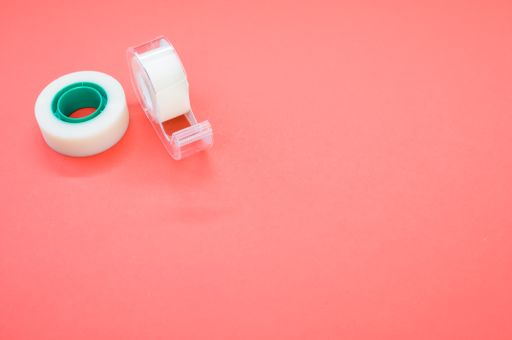 A top view closeup of a white duct tape and a tape dispenser isolated on a bright pink background