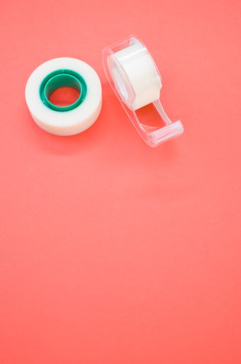A top view closeup of a white duct tape and a tape dispenser isolated on a bright pink background