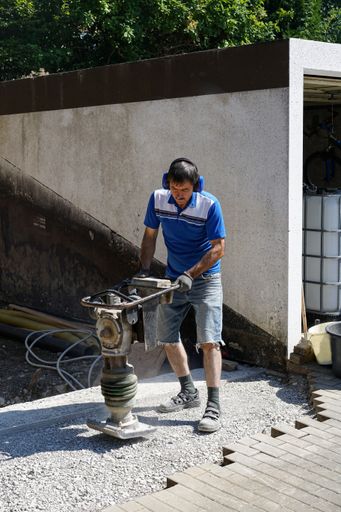A Caucasian construction worker compacting soil using a tamping rammer machine