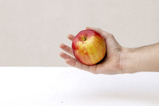 A high angle shot of an apple on a hand against the wall