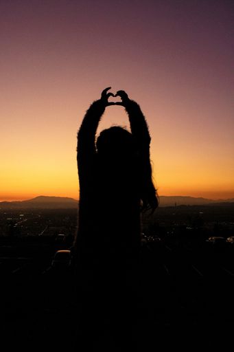 A vertical shot of a silhouette of a female making a heart shape with her hands during the sunset