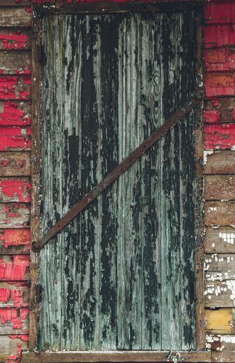 A vertical shot of the rusty door of an old wooden building with the remainings of the red paint