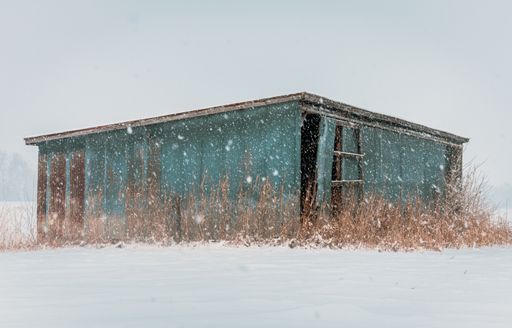 An old abandoned wooden blue hut in a deserted area during the snowflake
