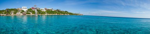A panorama of an island covered in buildings and greenery surrounded by the sea under a blue sky