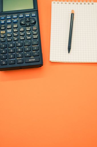 A top view closeup of a graphing calculator and a pen on a notepad  isolated on an orange background