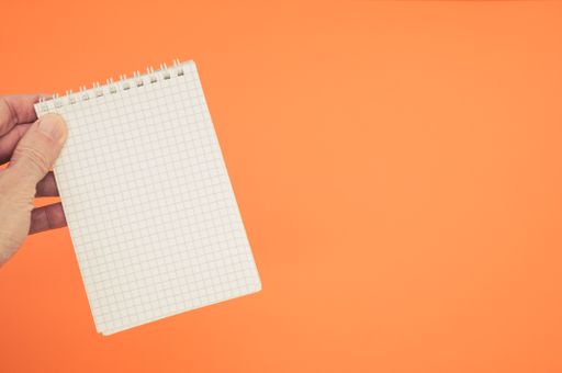 A top view closeup of a person holding a tiny notepad isolated on an orange background