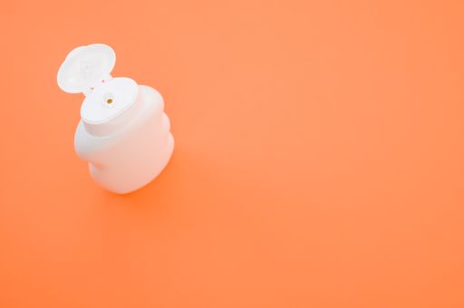A top view closeup of a bottle with an opened white cap isolated on an orange background