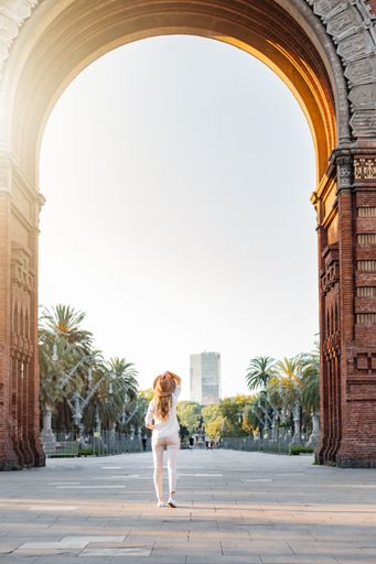 A shallow focus of a blonde female tourist with a fedora hat standing in Barcelona, Spain