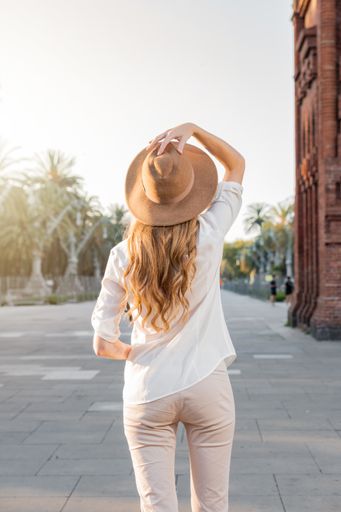A shallow focus of a young blonde tourist with a white shirt and a fedora hat posing in Barcelona, Spain
