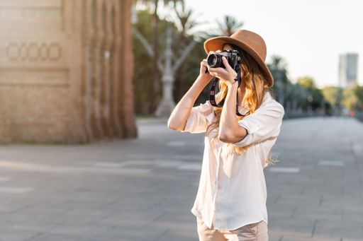 A shallow focus of a young female tourist with a fedora hat photographing in Barcelona, Spain